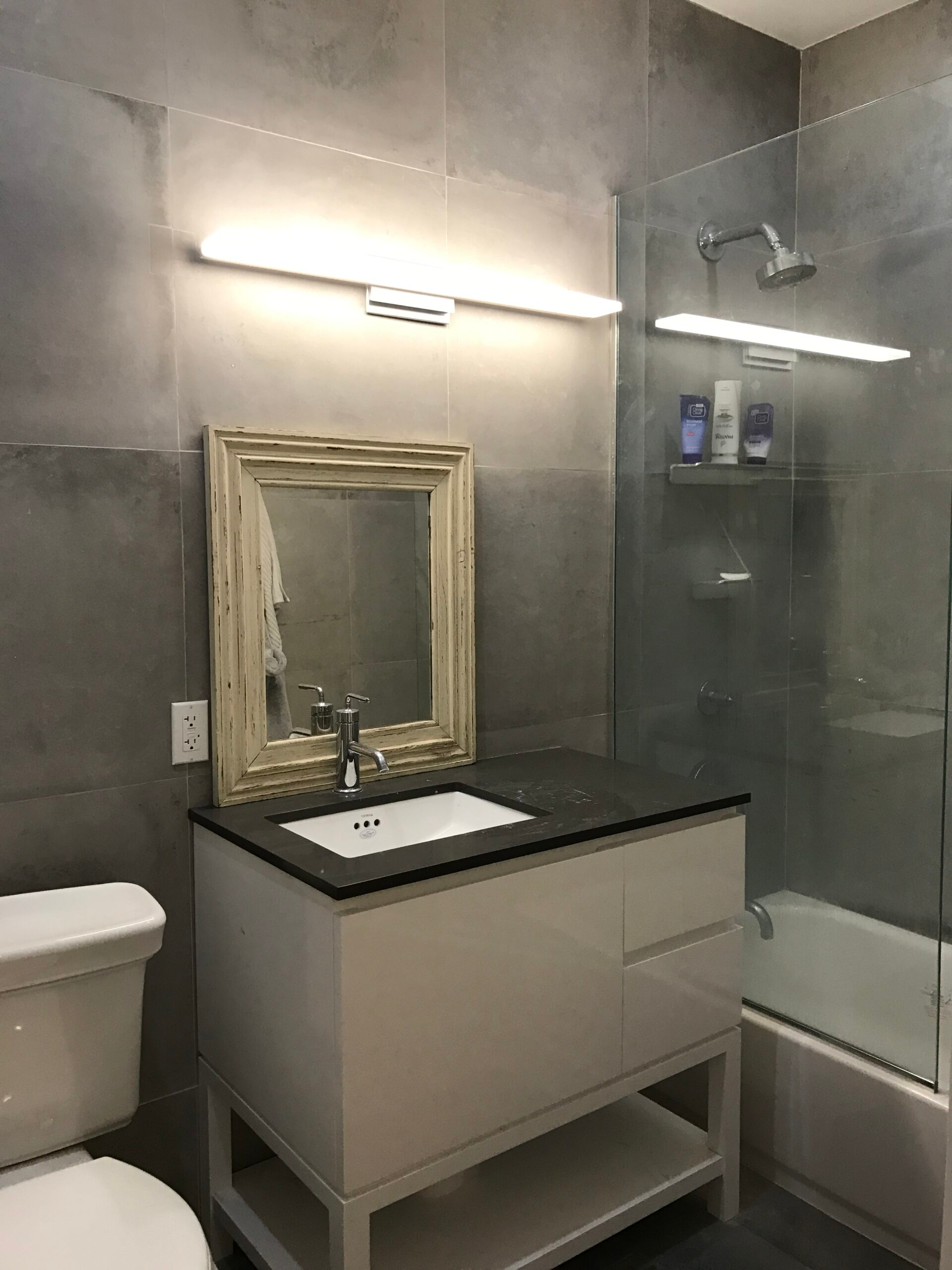 New York apartment bathroom with gray tile vanity and glass shower enclosure